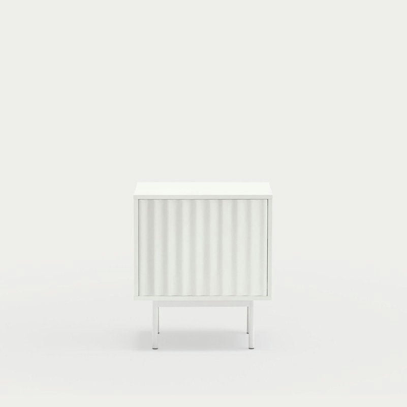 La mesita de noche Sierra 2C de Cambres Design es una mesa auxiliar minimalista blanca con un frente acanalado, una base de metal delgada y un fondo blanco liso para un almacenamiento elegante.