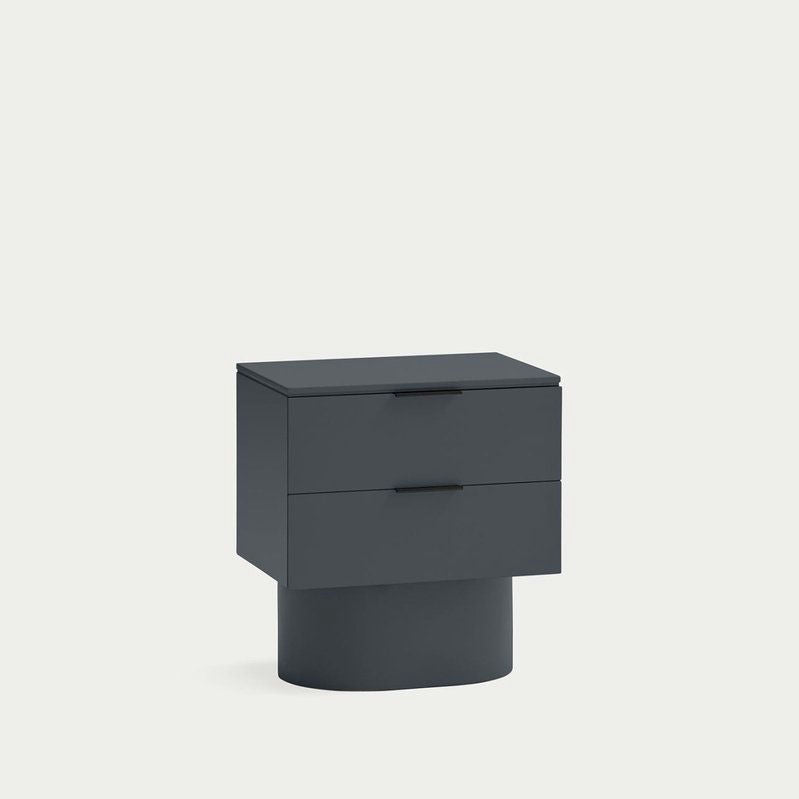 La Mesita de noche Totem 2C es una mesita de noche moderna de color verde oscuro con dos cajones, que cuenta con almacenamiento minimalista y una tapa rectangular sobre una base cilíndrica sobre un fondo gris claro, lo que la convierte en un epítome del diseño contemporáneo.