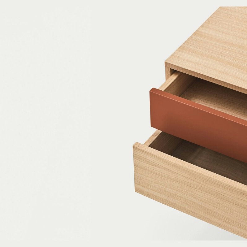 La mesita de noche Yoko 2C de Cambres Design presenta una cajonera de madera con un cajón abierto, que muestra un espacio vacío en el interior. El frente de color marrón rojizo contrasta hermosamente con el acabado de madera clara, lo que refleja un diseño contemporáneo, todo sobre un fondo blanco liso.