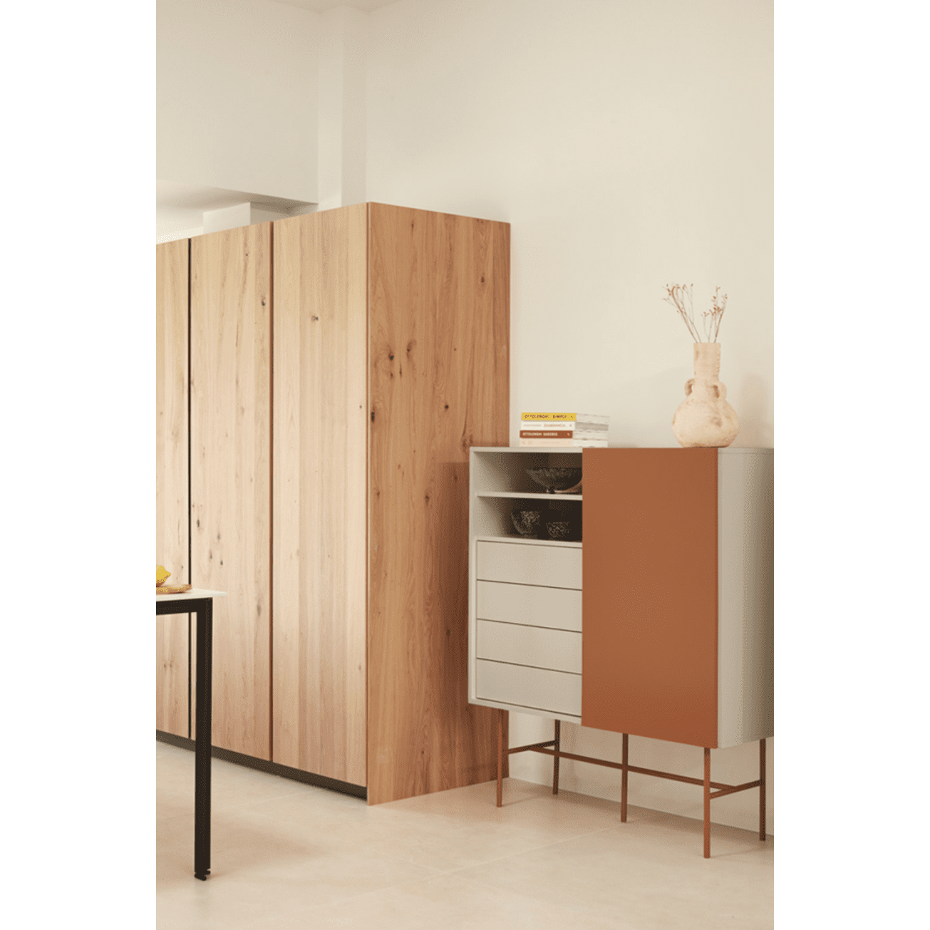 Interior moderno con un armario de madera y el Aparador con Puerta Corredera y Cajones Nube 1P4C, con puertas corredizas para un fácil acceso. Un jarrón y libros adornan este diseño minimalista. Las paredes y los pisos neutros realzan el aspecto elegante del mueble auxiliar.