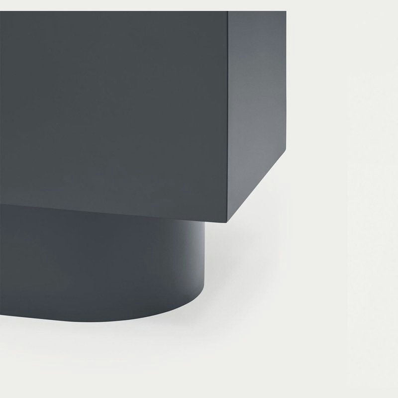 Primer plano del Aparador moderno con Puertas Totem 2P, mostrando su diseño geométrico gris oscuro con una parte superior rectangular y una base cilíndrica sobre un fondo claro, encarnando el minimalismo.