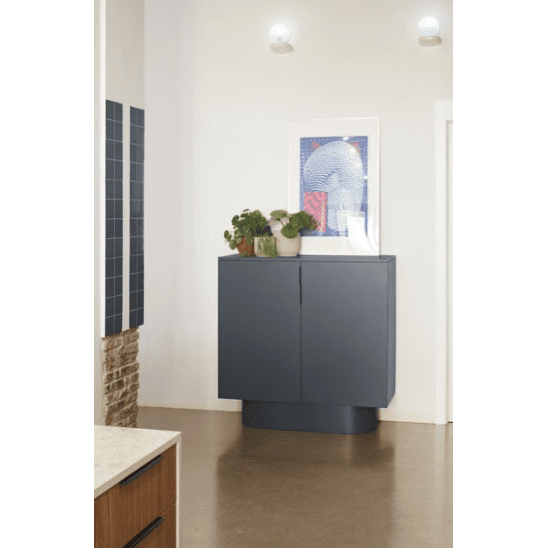 El Aparador moderno con Puertas Totem 2P en gris oscuro se destaca contra una pared clara, decorada con plantas en macetas y obras de arte enmarcadas, capturando el minimalismo bajo dos apliques de pared circulares.