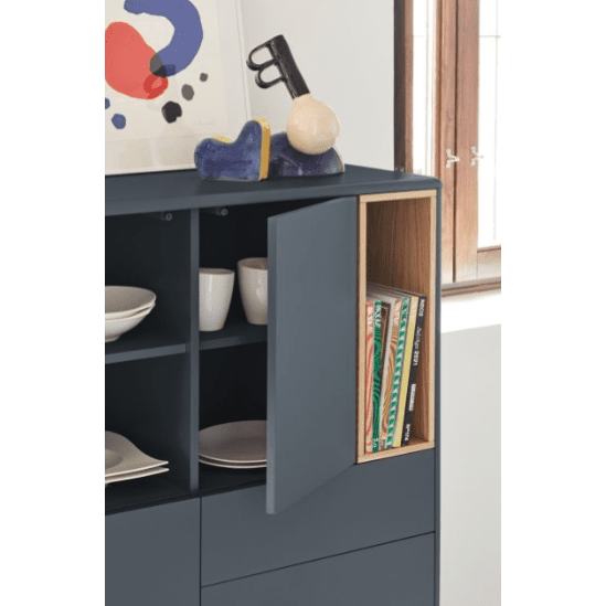 El Mueble Auxiliar con Puertas y Cajones Corvo 3P3C, en azul vibrante, presenta estanterías innovadoras para exhibir libros y vajillas. Rematado con una moderna escultura de arma junto a una ventana, combina a la perfección almacenamiento innovador con decoración contemporánea.
