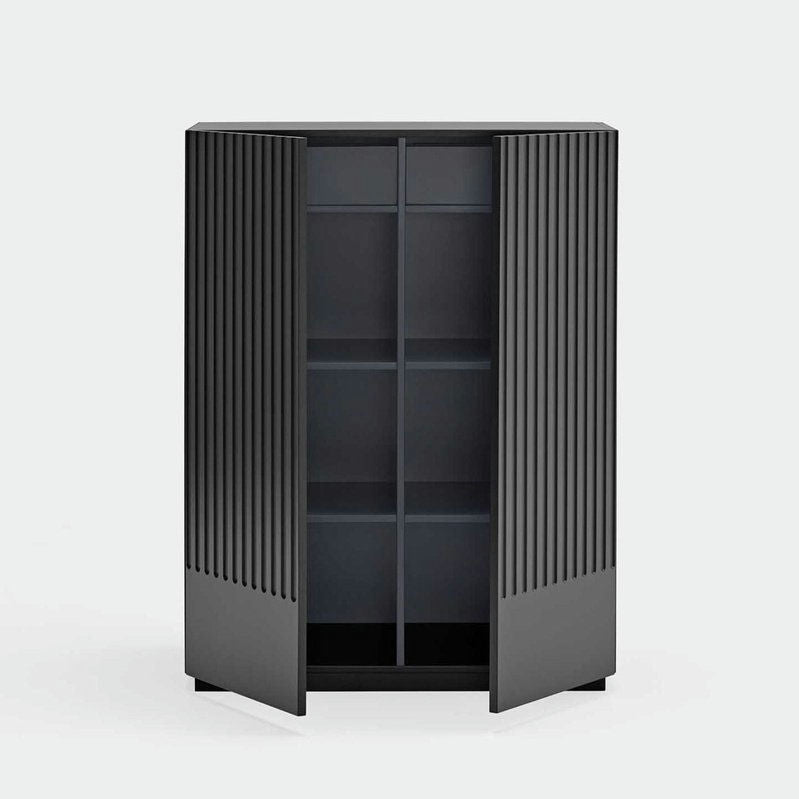 El Aparador pequeño con puertas Doric 2P2C, un mueble alto de color gris oscuro con ranuras verticales características en sus puertas entreabiertas, revela dos estantes que forman cuatro compartimentos. Se destaca sobre un fondo gris claro y ofrece una elegancia moderna a cualquier habitación.