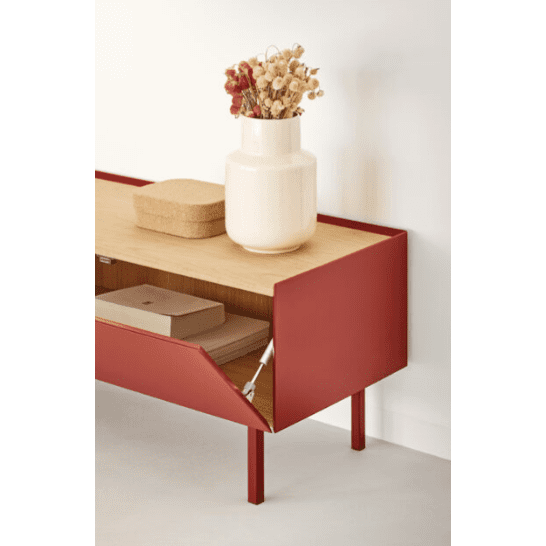 El Mueble TV Arista 1P2C, en un rojo intenso, personifica el diseño moderno contra una pared blanca y un piso claro. Su puerta abierta muestra libros en el interior, lo que brinda un almacenamiento sofisticado. Un gran jarrón blanco con flores secas y una pequeña caja tejida se encuentran encima, lo que agrega encanto y elegancia.