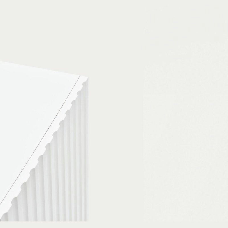 Primer plano de la esquina del Mueble TV Doric 4P2C sobre un fondo liso, resaltando su textura de cartón corrugado blanco y el detalle de sus bordes que recuerdan al diseño clásico.