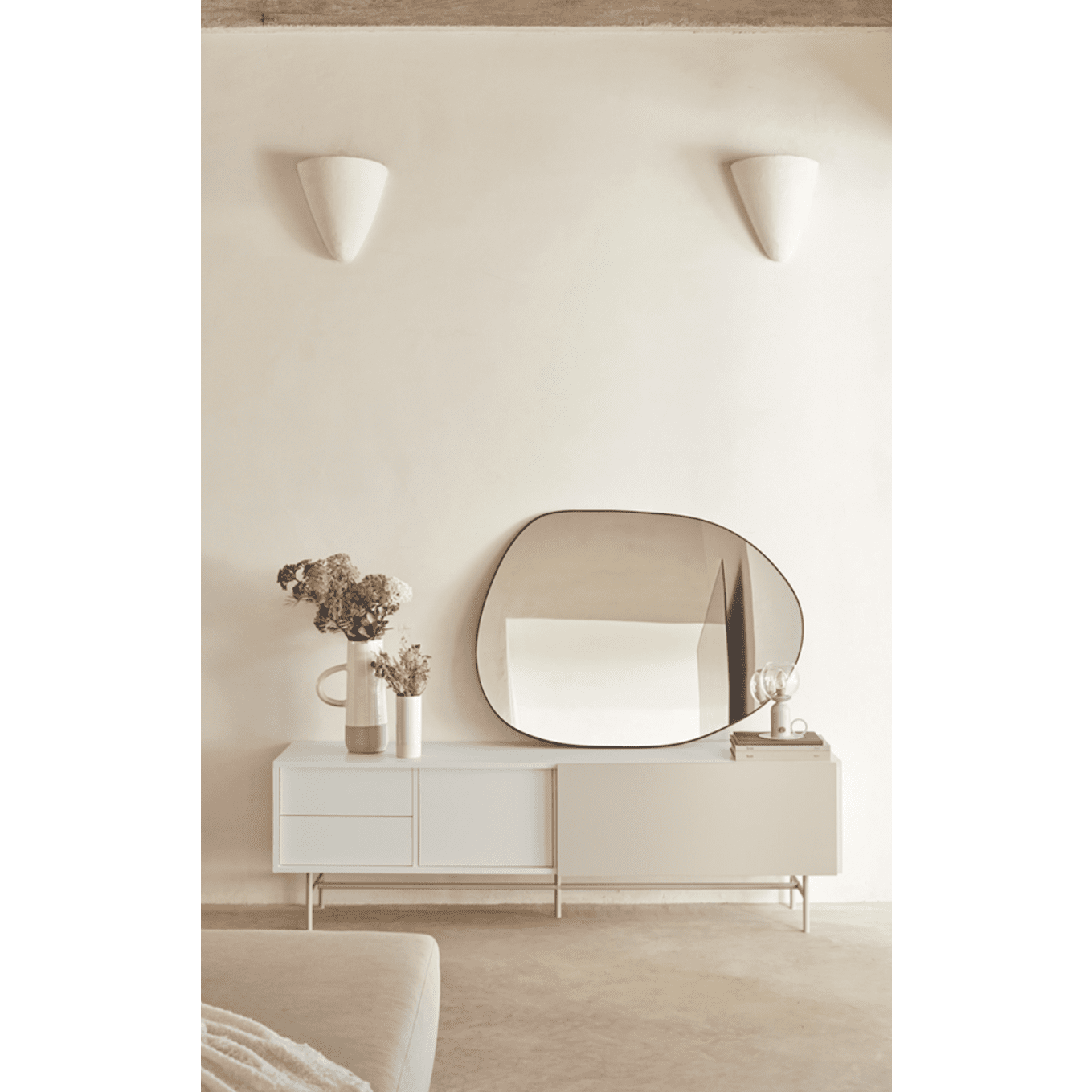 El interior minimalista incluye el Mueble TV Nube 2P2C, un espejo asimétrico y un jarrón de flores secas contra una pared neutra con dos apliques, lo que proporciona una personalización única.