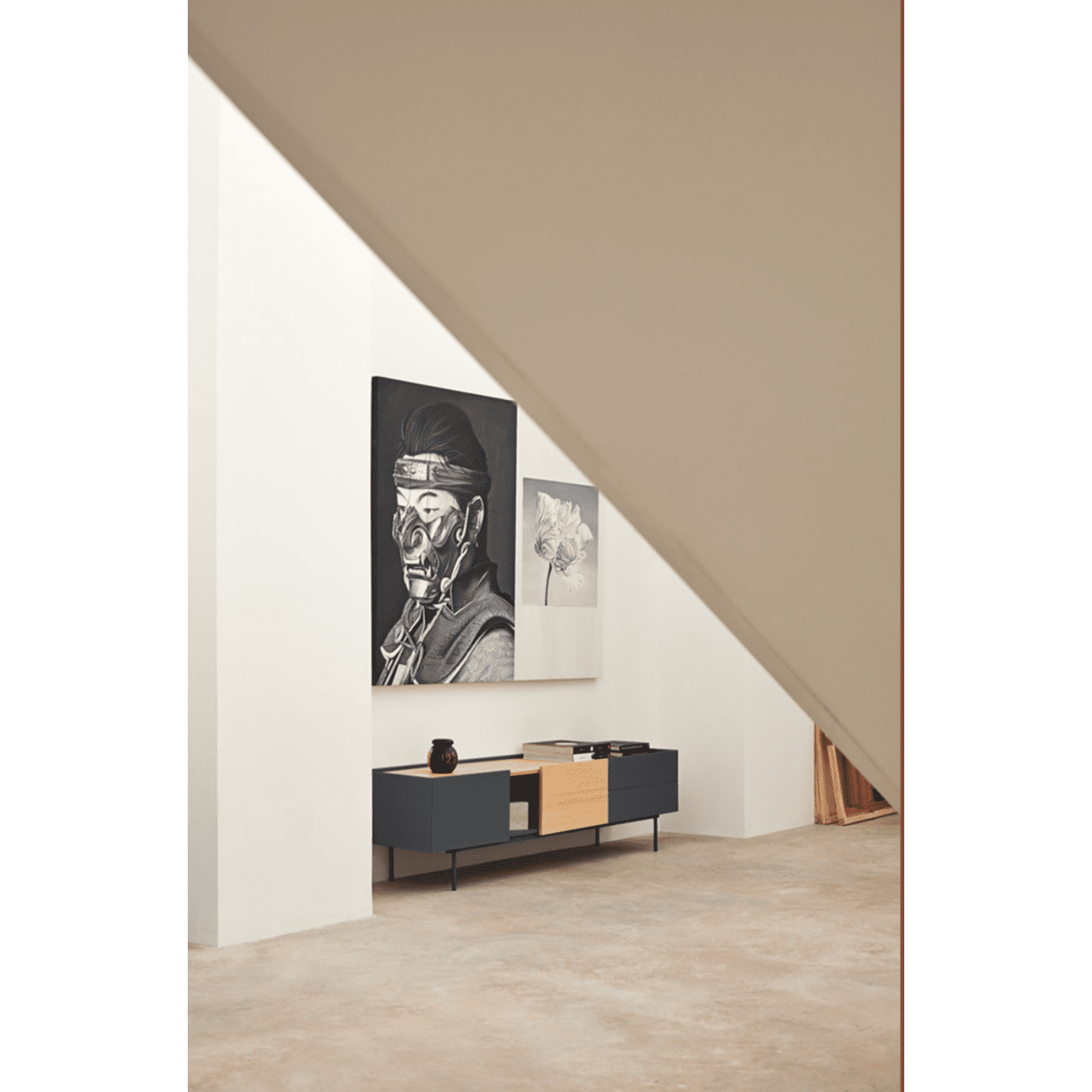 En un interior moderno, el elegante Mueble TV Otto 2P2C funciona como un elegante aparador negro. Sobre él, una pintura abstracta y otra que representa a una persona con marcas faciales adornan las paredes beige. La decoración minimalista crea un diseño contemporáneo limpio con una integración perfecta de almacenamiento y multimedia.