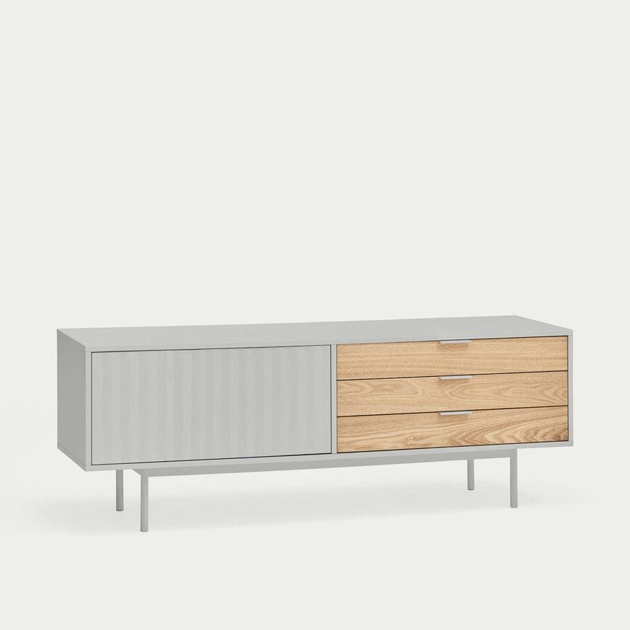 El Mueble TV Sierra 1P3C es un aparador moderno con una puerta corrediza gris a la izquierda, tres cajones de madera a la derecha y delgadas patas de metal, que muestra un almacenamiento elegante con su diseño asimétrico.