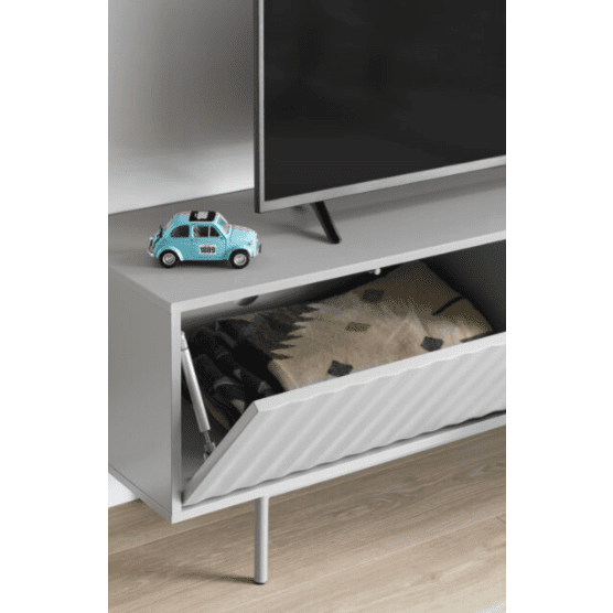 El Mueble de TV Sierra 1P3C, un elegante mueble blanco con un compartimento abierto para mantas dobladas, ofrece un almacenamiento elegante. Un modelo en miniatura de un automóvil azul junto a un televisor de pantalla plana acentúa su atractivo moderno.