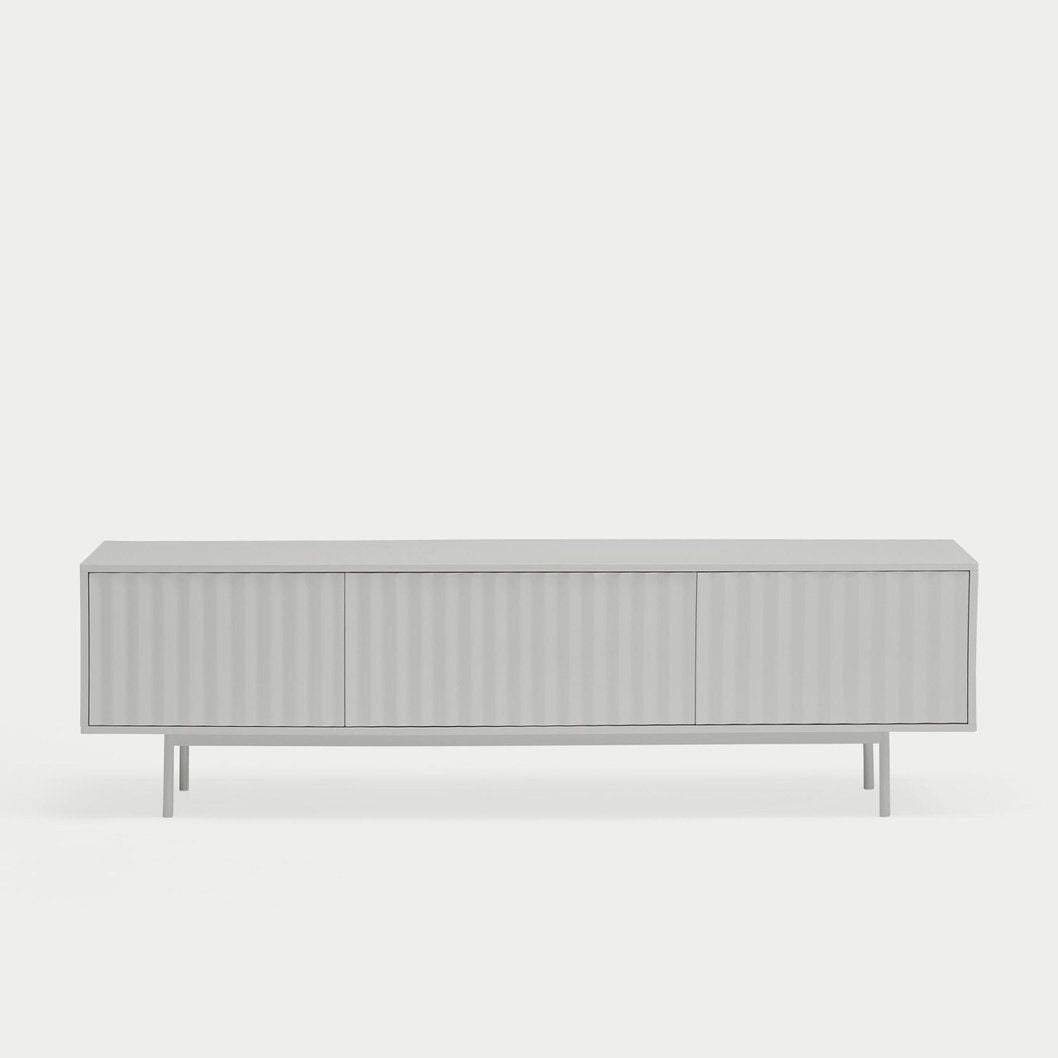 El Mueble TV Sierra 3P es una consola multimedia minimalista de color gris claro con un frente texturizado y patas delgadas que encarnan el diseño modernista. Se destaca sobre un fondo simple y combina a la perfección estilo y funcionalidad para un almacenamiento multimedia perfecto.