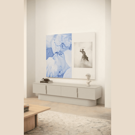 Una habitación minimalista muestra el Mueble TV Totem 4P beige, que ofrece un espacio de almacenamiento moderno debajo de obras de arte abstractas en blanco y negro. Una escultura de cabeza y un teléfono antiguo se encuentran elegantemente sobre él, con parte de una mesa de café visible cerca.