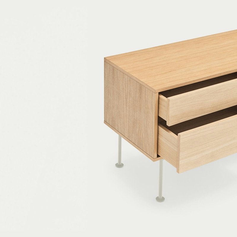 El Mueble TV Yoko 1P2C, un aparador de madera con dos cajones parcialmente abiertos, se presenta sobre un fondo liso. Está elevado sobre patas de metal cortas y delgadas para lograr un diseño contemporáneo y ofrece un almacenamiento elegante.