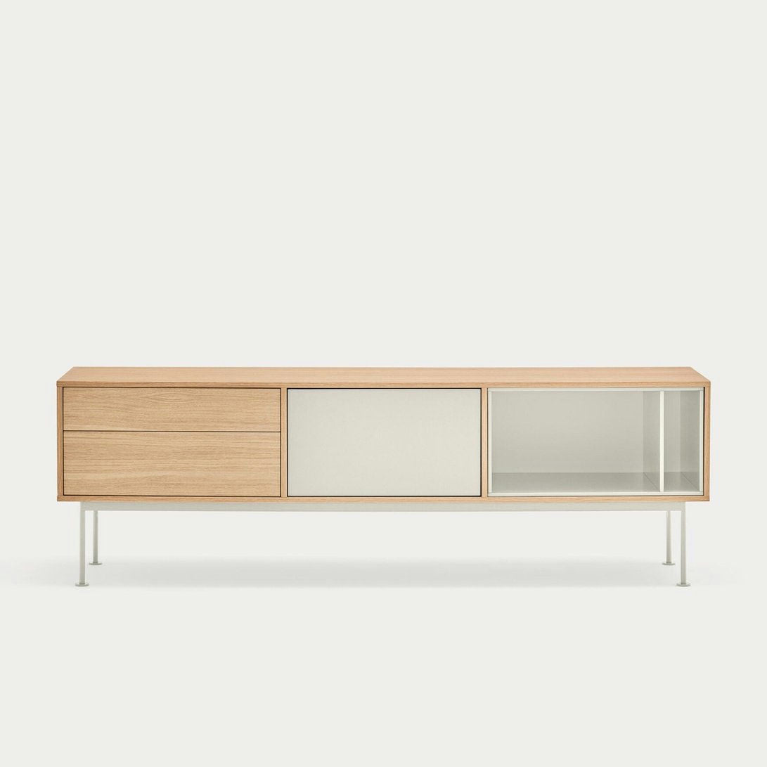 El Mueble TV Yoko 1P2C es un aparador minimalista de madera con un diseño contemporáneo, que cuenta con dos cajones en el lado izquierdo, un panel central de vidrio esmerilado y una sección de vidrio transparente a la derecha, todo elegantemente sostenido por patas de metal blanco.