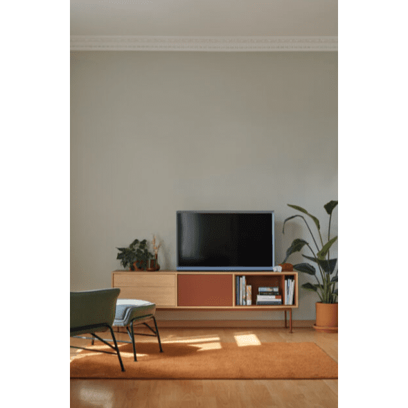 La sala de estar presenta un diseño contemporáneo con un elegante televisor Mueble TV Yoko 1P2C sobre un mueble de madera, complementado con una silla verde y una planta de interior. Los libros adornan el elegante estante de almacenamiento, mientras que una alfombra naranja aporta calidez al piso de madera clara.