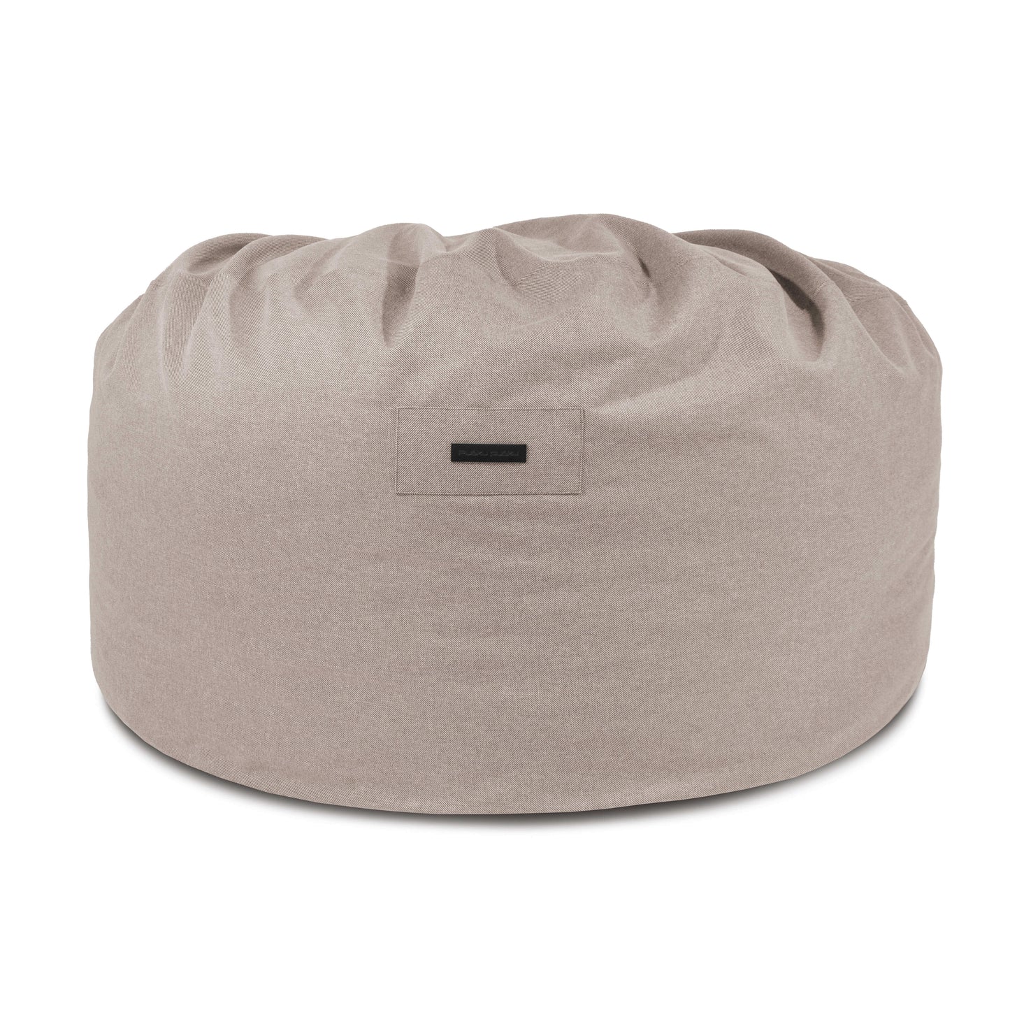 El Foam Bean Bag Om 135 Riviera -grande, redondo y de color beige claro con una pequeña etiqueta frontal- ofrece un asiento cómodo para relajarse en cualquier espacio exterior.