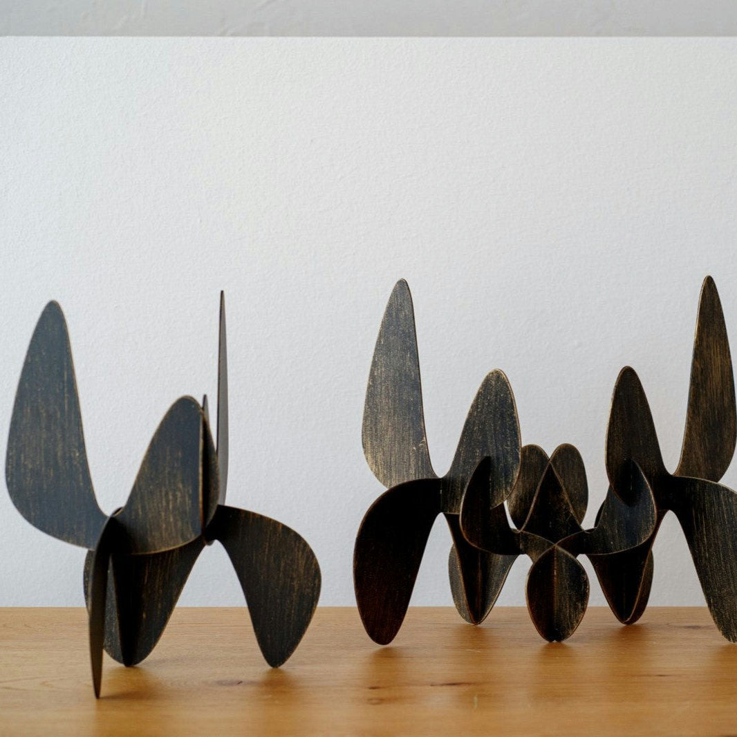 Figuras Decorativas en Metal Orgánico Lámina Oro muestra formas curvas y superpuestas sobre una superficie de madera, realzadas por delicados detalles en lámina oro, combinando sin esfuerzo naturaleza y arte.