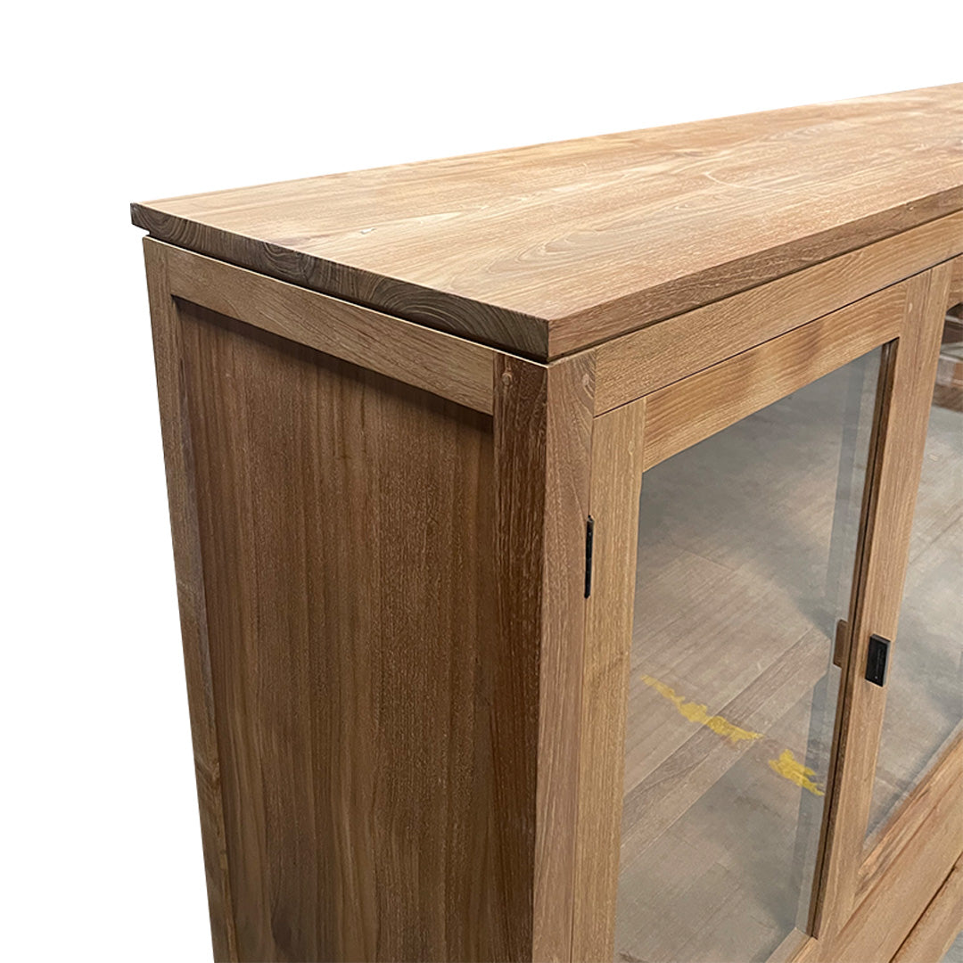 El Aparador en Madera de Teca Begur ofrece una solución de almacenamiento refinada con su gabinete de madera, dos elegantes puertas de vidrio y una superficie lisa, bellamente exhibida desde una vista de esquina frontal.