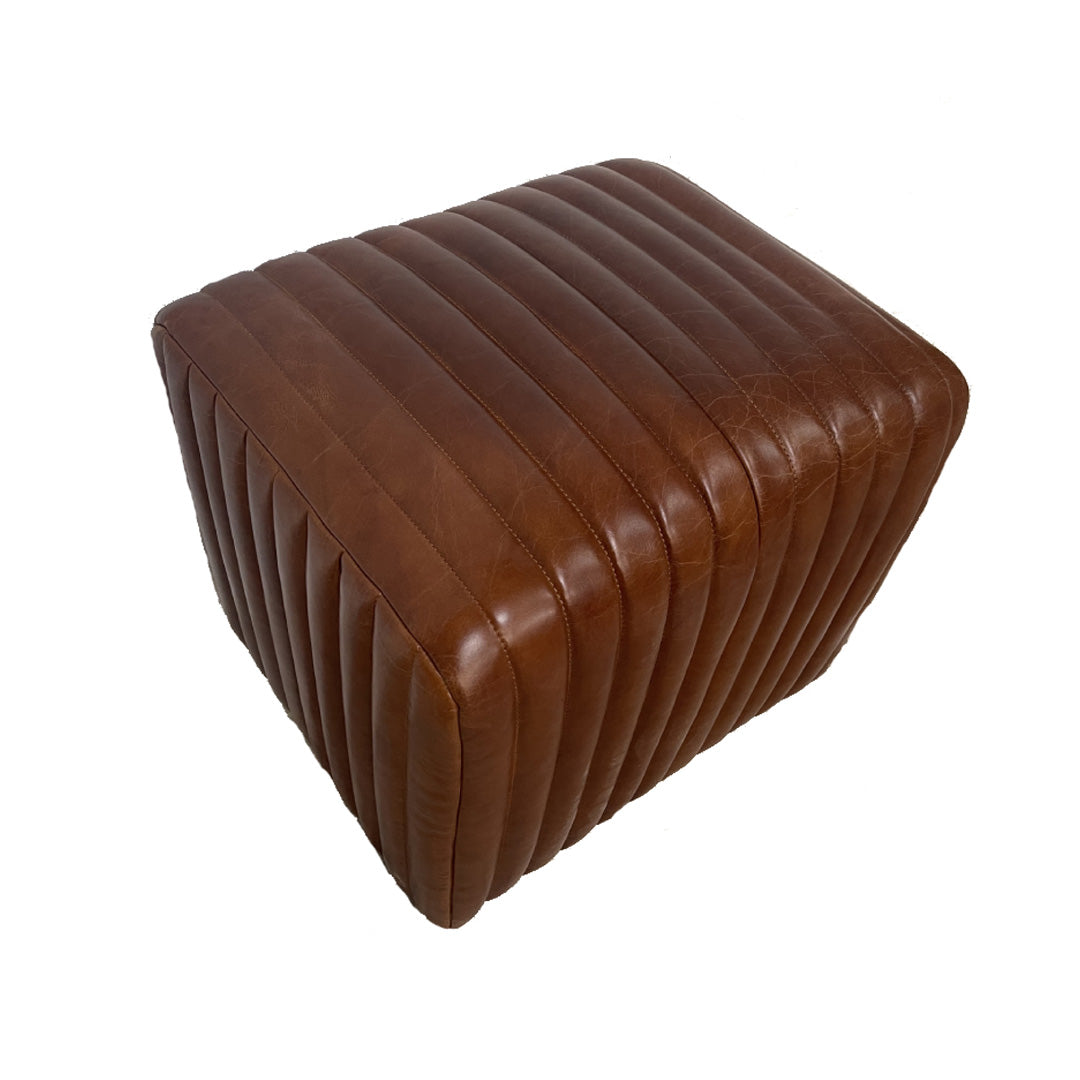 El puf cuadrado Bristol, elaborado en piel marrón con un diseño rectangular acanalado, es ideal para espacios modernos. Se presenta sobre un fondo blanco liso.
