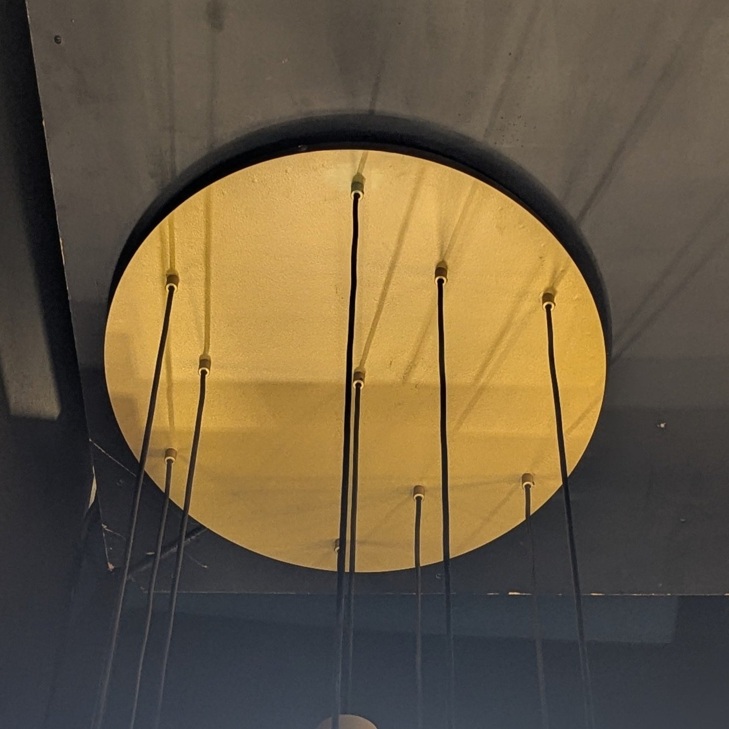 Primer plano de la Lámpara de techo en acero y vidrio Gold Ball 10, una lámpara de techo redonda de color amarillo con varios cables negros sobre un fondo oscuro.