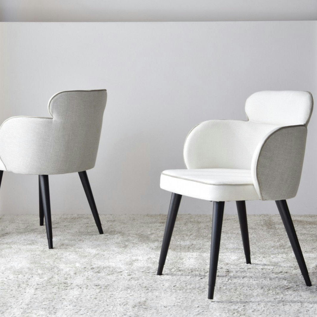 Una alfombra texturizada en esta habitación minimalista está adornada por dos sillas de comedor Oslo, con tapizado claro, patas de madera oscura y apoyabrazos, capturando la esencia del diseño escandinavo.