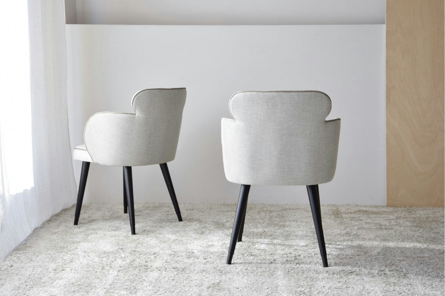 Paquete de dos Sillas de Comedor Tapizadas con Reposabrazos Oslo, con un moderno diseño gris con patas negras, colocadas sobre una alfombra de textura clara en una habitación minimalista, que incorpora el diseño escandinavo.