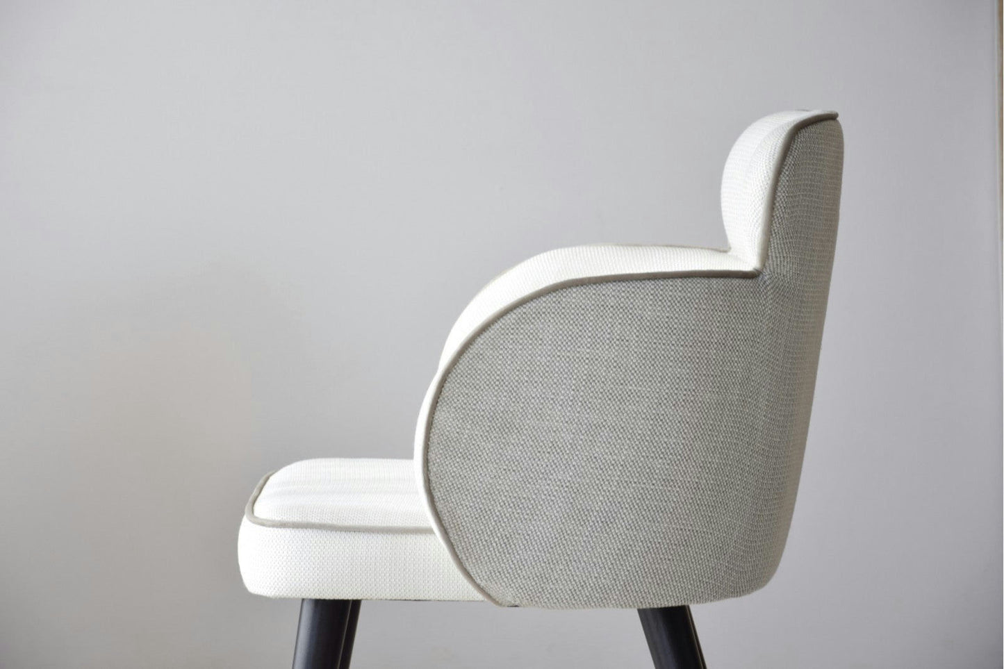 Vista lateral de una elegante silla tapizada en gris claro con patas negras, similar a las Sillas de Comedor Tapizadas con Reposabrazos Oslo, sobre un fondo blanco liso.
