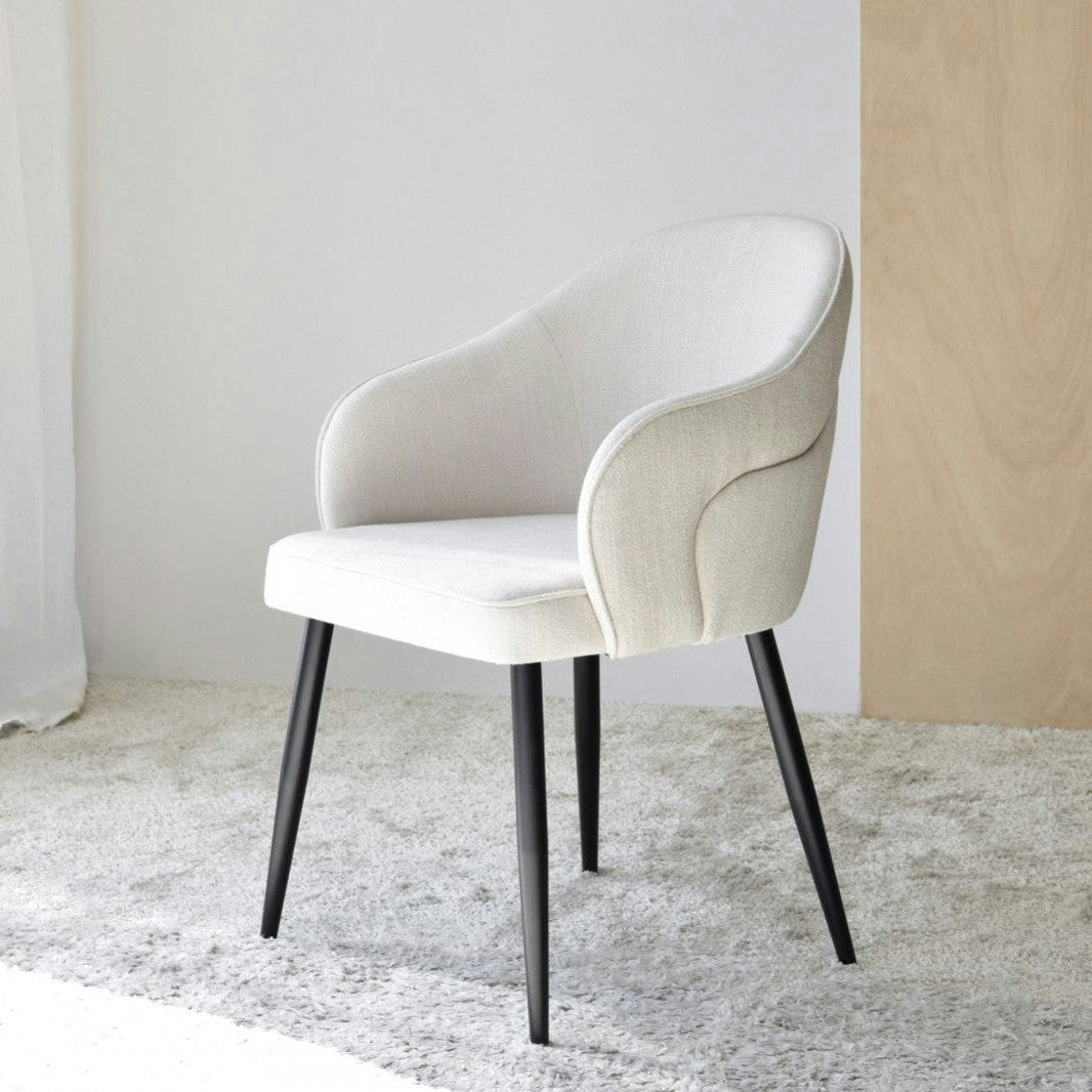 El Pack 2 Sillas de Comedor con Reposabrazos Roma (Beige claro) cuenta con modernas sillas tapizadas con respaldos curvos y patas de metal negro, que descansan sobre una alfombra clara. Ideales para el Estilo Contemporáneo, combinan el Diseño Ergonómico con una estética elegante para tu comedor.