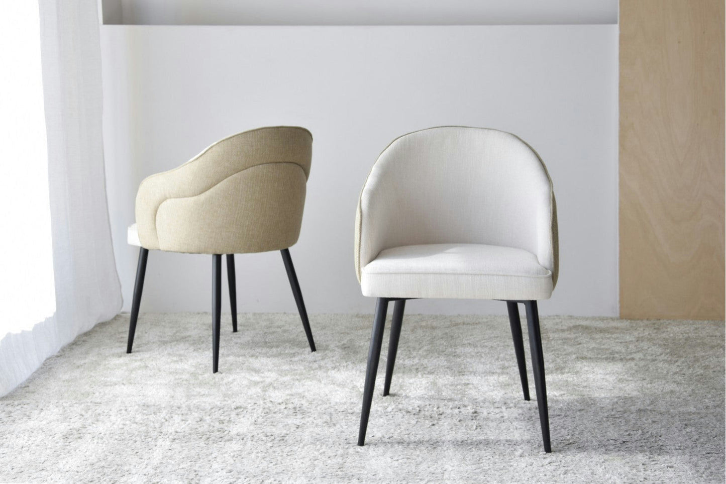Un paquete de 2 sillas de comedor Roma con respaldos curvos tapizados en beige y patas negras metálicas están elegantemente colocadas sobre una alfombra gris claro en una habitación bien iluminada.