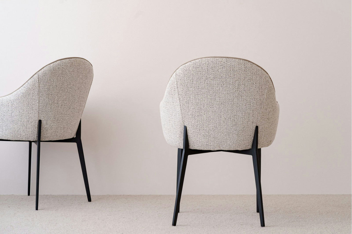 Las sillas Pack 2 Sillas de comedor tapizadas Beige y Gris Elna, con tapizado beige moderno y patas de metal negro, se destacan elegantemente sobre un fondo blanco liso, personificando el diseño contemporáneo.