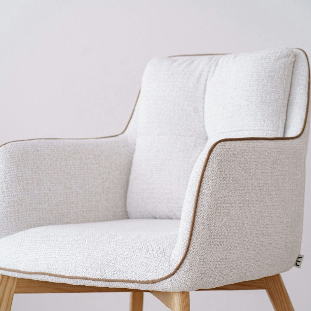 El Pack 2 Sillas de comedor tapizadas Marfil Oliver, con un diseño de estilo escandinavo en color blanco con patas de madera clara y ribetes marrones, complementa a la perfección un fondo claro y liso.