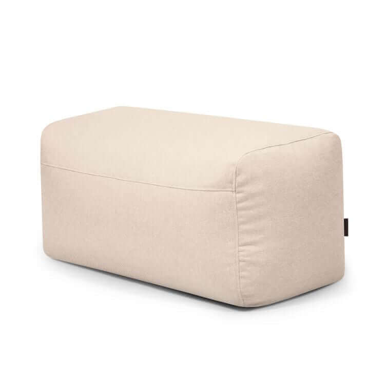El Pouf Plus 100 Riviera es una otomana rectangular de color beige con suave tapicería de tela y bordes lisos, que ofrece un reposapiés versátil para uso en exteriores, mostrado sobre un fondo blanco liso.