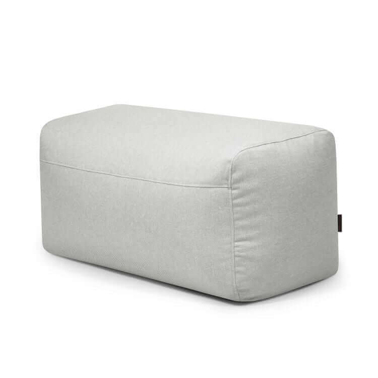 Puf Plus 100 Riviera rectangular gris claro para uso exterior, con bordes redondeados; sirve como reposapiés versátil o asiento extra, mostrado sobre un fondo blanco liso.