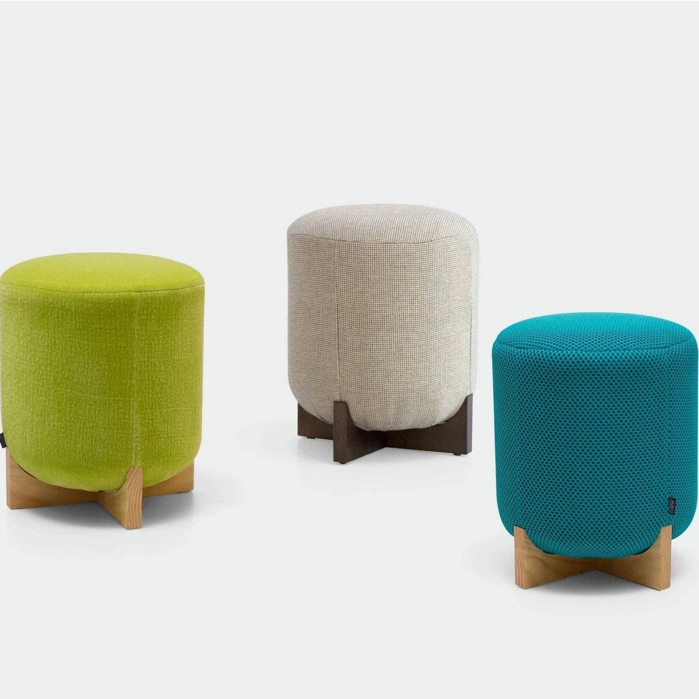 Tres pufs Puff Redondo Tapizado Kryss con patas de madera se asientan elegantemente sobre un fondo claro y muestran un diseño moderno. Estas piezas son de color verde, beige y verde azulado y ofrecen opciones de mobiliario personalizables para cualquier espacio habitable con estilo.