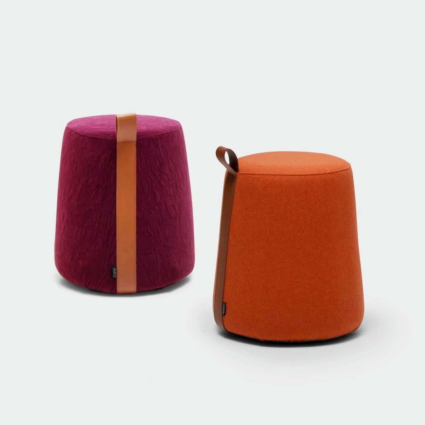 Los taburetes Puff Redondo Tapizado Ringe, de diseño moderno con tiradores de piel, vienen en magenta y naranja. Ideales para ambientes de mobiliario de empresa, aportan color y estilo vibrantes a cualquier espacio sobre un fondo gris claro.