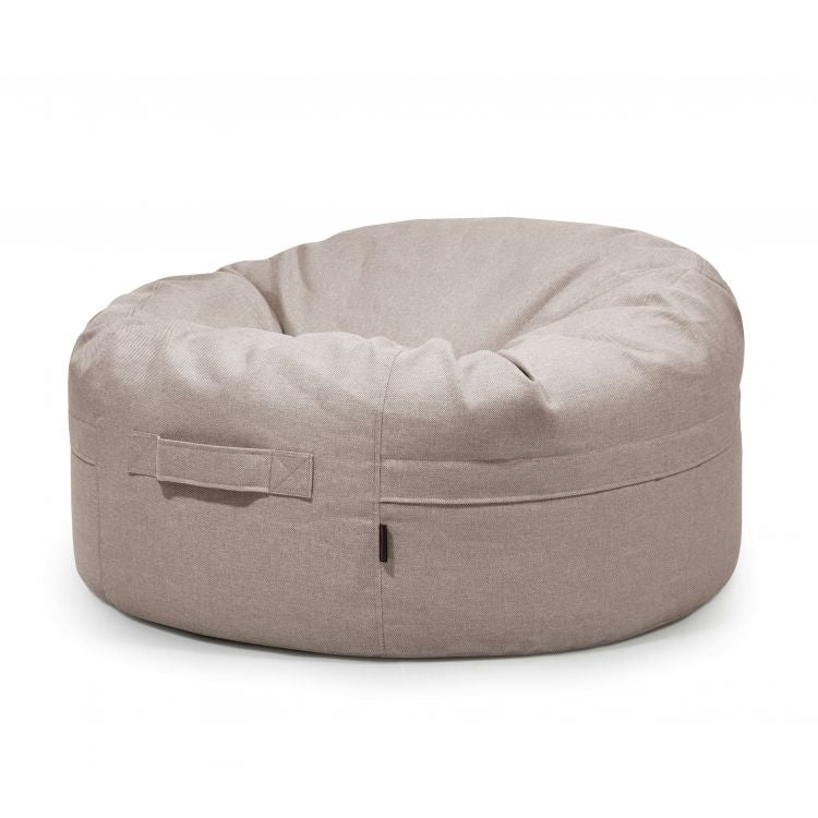 El Bean bag Roll 105 Riviera - uso exteriores es un puff moderno redondo de color beige claro con asa lateral, ideal como puff para niños, que se presenta sobre un fondo blanco liso.