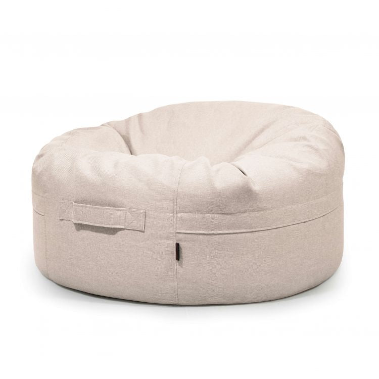 Un Bean bag Roll 105 Riviera de color beige para uso exterior, con asa lateral, se coloca sobre un fondo blanco, proporcionando un acogedor y moderno puff para niños.