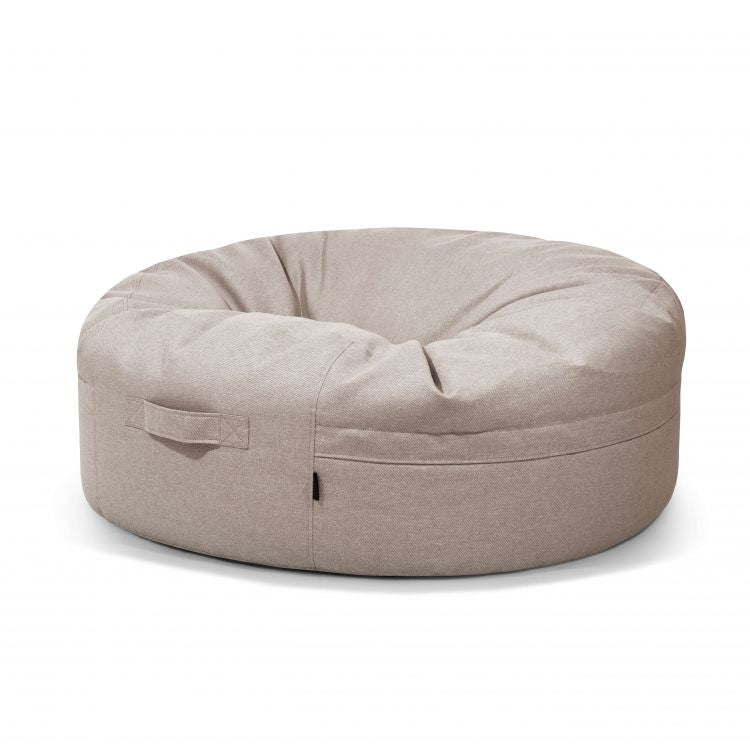 El Bean Bag Roll 135 Riviera es un puff redondo de color beige con asa lateral, perfecto para sentarse cómodamente al aire libre y elegantemente presentado sobre un fondo blanco.