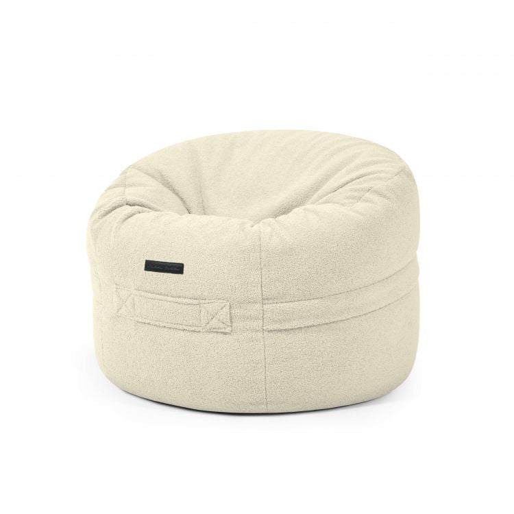 El ROLL 80 TEDDY es un puf redondo de borreguito blanco roto (80×80×35 cm) con tejido texturizado y asa lateral cosida, perfecto para el salón o el dormitorio.