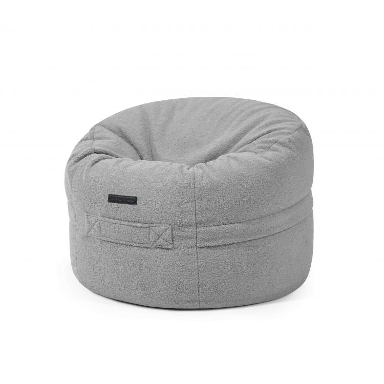 El ROLL 80 TEDDY es un Puff redondo de borreguito (80×80×35 cm) de color gris claro, con tapa blanda y asa lateral, perfecto para tu salón o dormitorio, que se muestra sobre un fondo blanco liso.