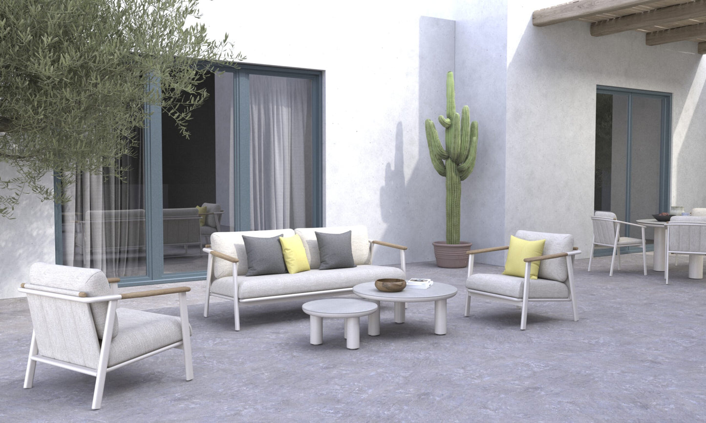 Moderno patio exterior con mobiliario de color claro, en el que destaca el Sofá de exterior 3 plazas en aluminio y teca - gris arena (189×82×71cm - SAND), mesas redondas, cactus en macetas y grandes puertas correderas de cristal contra una pared blanca.
