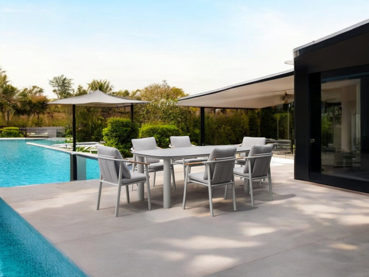 Zona de comedor exterior con una Mesa de comedor de exterior rectangular en porcelánico -220x100x78cm- ARENA y seis sillas en un moderno patio junto a la piscina, rodeado de vegetación y arquitectura contemporánea.