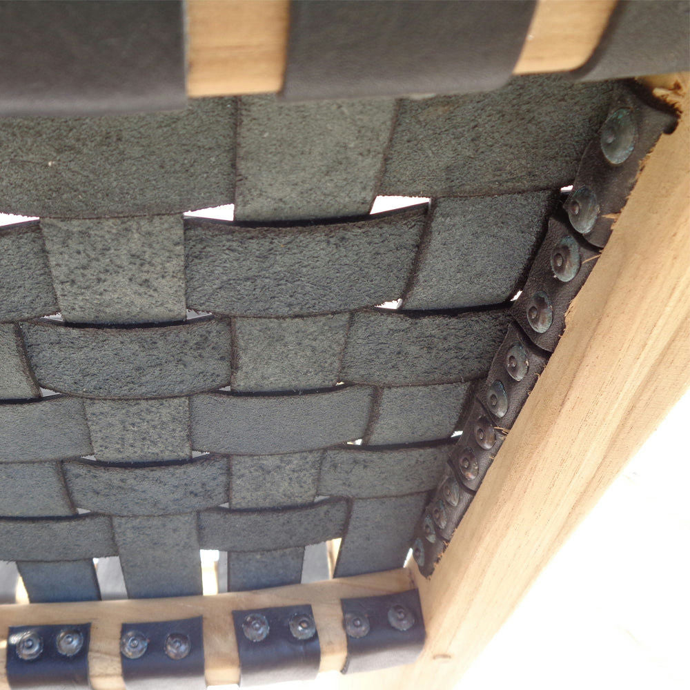 Primer plano del asiento de la silla SILLA ZOE BLACK, que presenta correas tejidas negras elaboradas a partir de teca y unidas a un marco de madera mediante remaches.