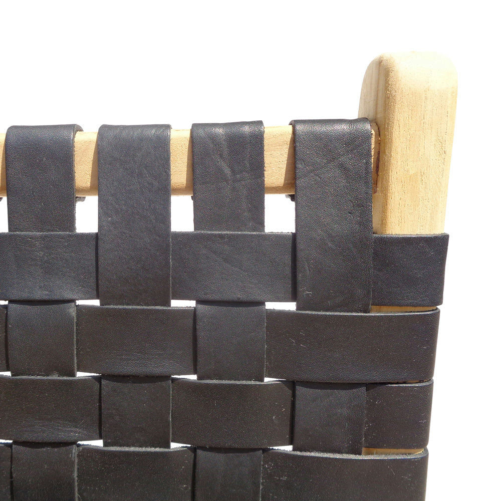 Primer plano de la SILLA ZOE BLACK mostrando sus correas tejidas en negro y un marco de madera de teca clara.