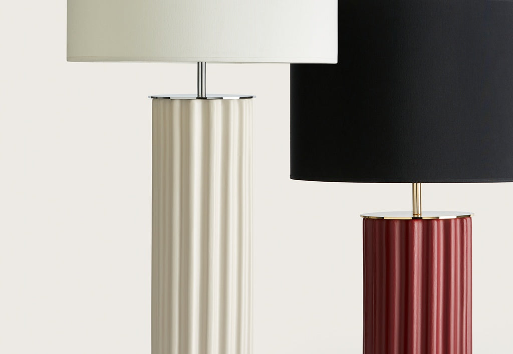 Dos Lámparas de mesa en Cerámica y Metal Sonica -una beige con pantalla blanca y otra roja con pantalla negra- crean un elegante acento decorativo sobre un fondo liso.