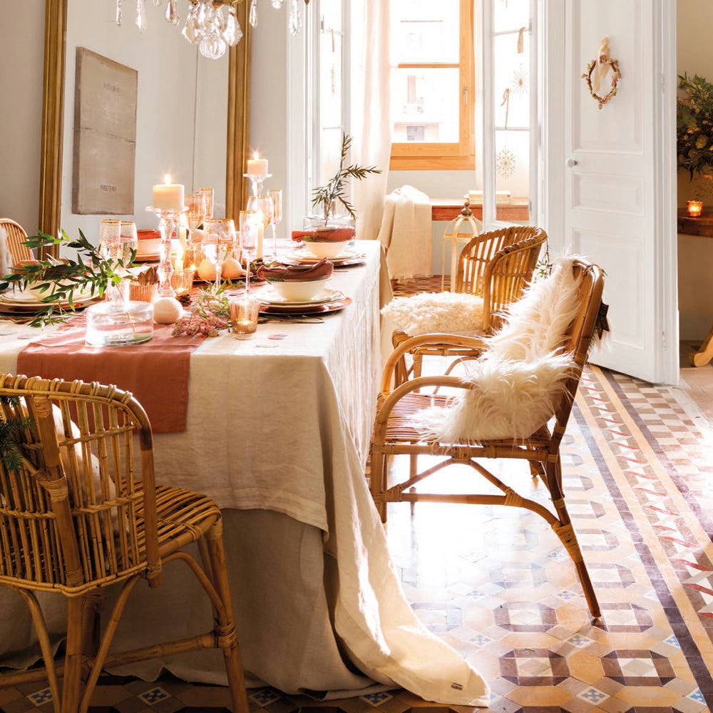 Mesa de comedor elegantemente dispuesta con velas y vegetación en una habitación luminosa que presenta la Silla de comedor en bambú y ratán Robert, complementada con baldosas estampadas en el piso, adoptando un encantador diseño rústico.