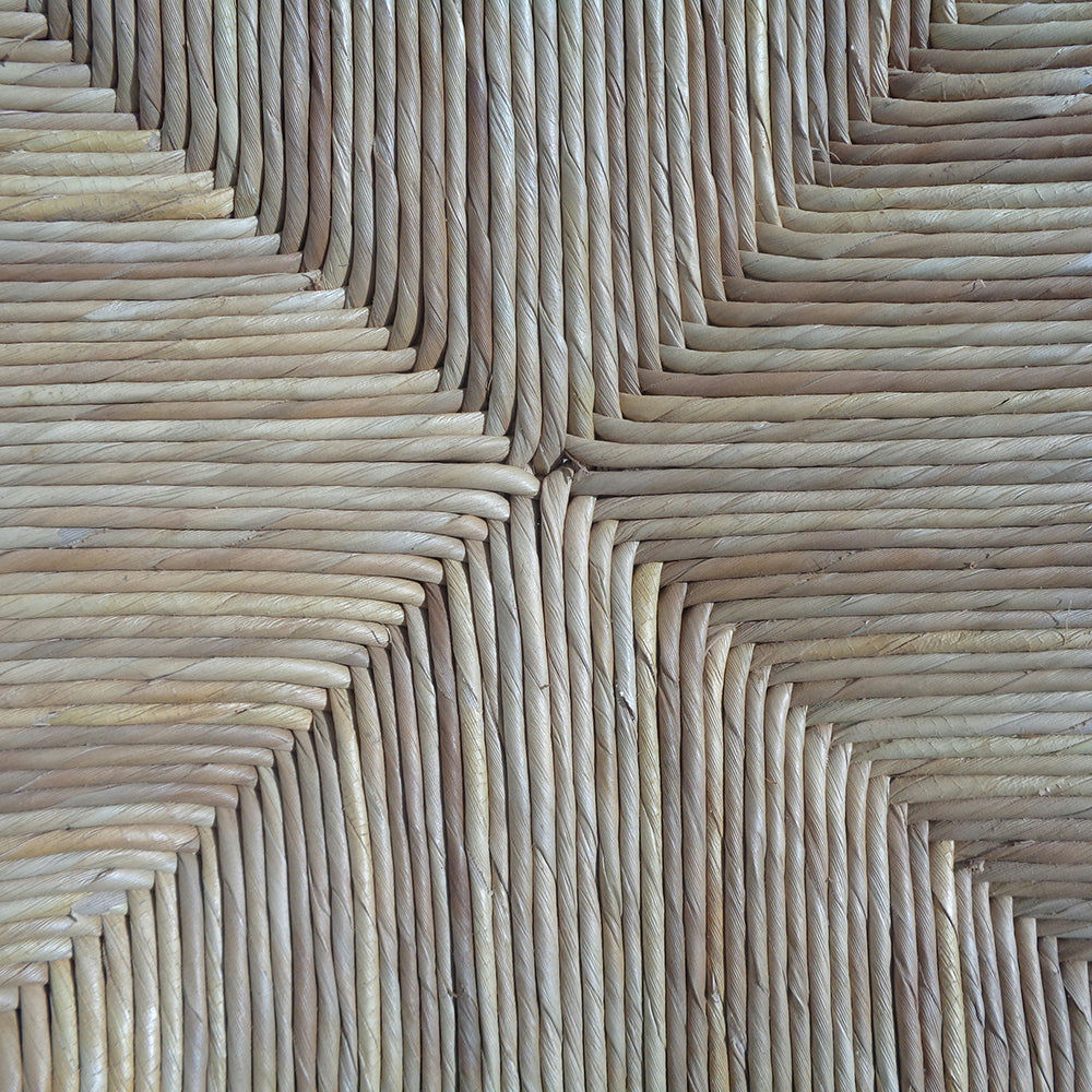 Primer plano de un patrón de mimbre tejido elaborado con fibra de banano, con formas simétricas de diamantes. El diseño texturizado evoca la elegancia de una silla de comedor en madera y fibra Tulum.