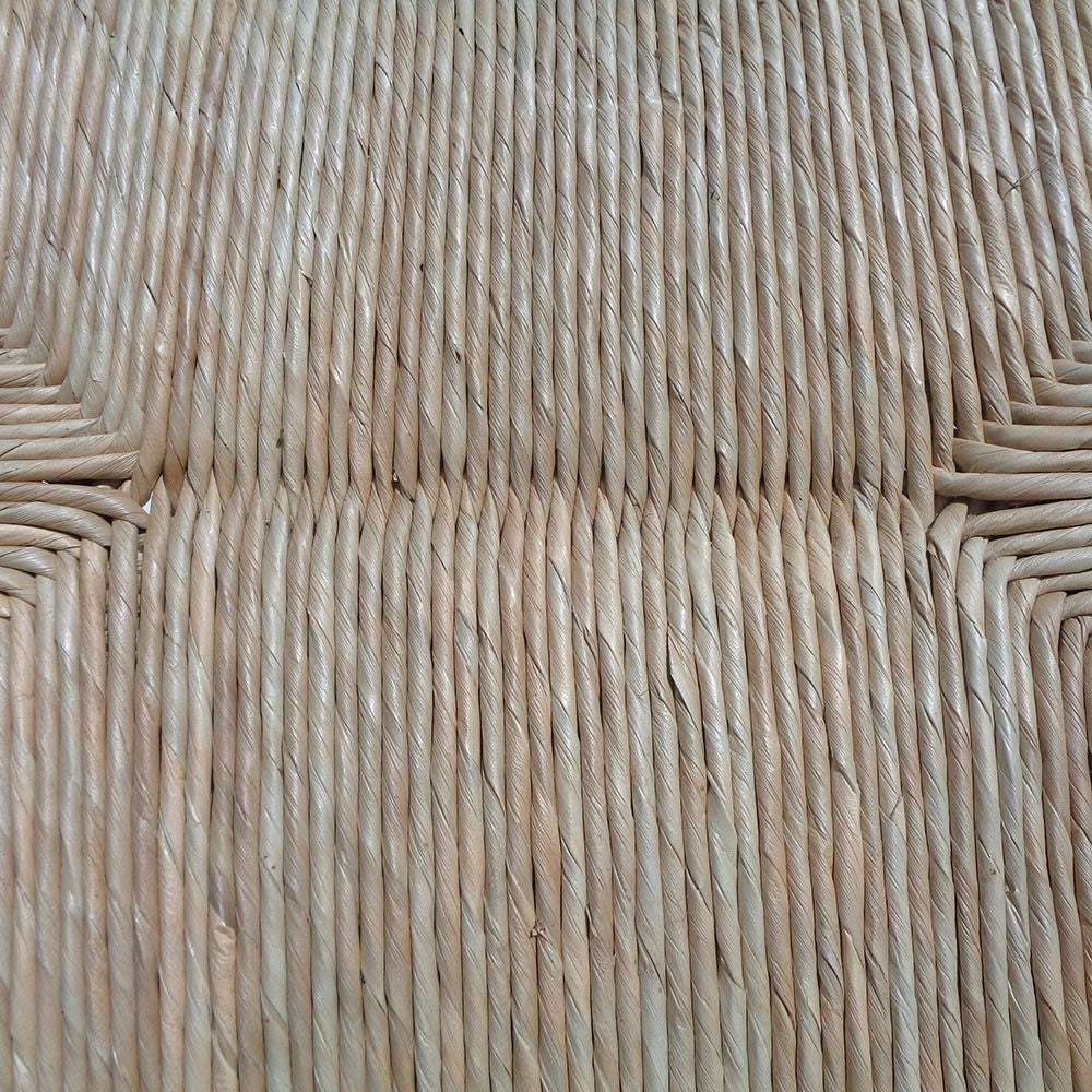 Primer plano de un diseño de paja tejida con líneas diagonales entrecruzadas en tonos beige naturales, que recuerda la intrincada artesanía que se encuentra en la Silla de comedor madera teca Zoe Banana.