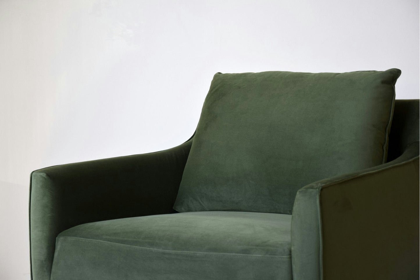Un Sillón de Diseño en Terciopelo Ntsu en terciopelo verde oscuro contrasta elegantemente con un fondo gris claro, realzado por elegantes patas metálicas.