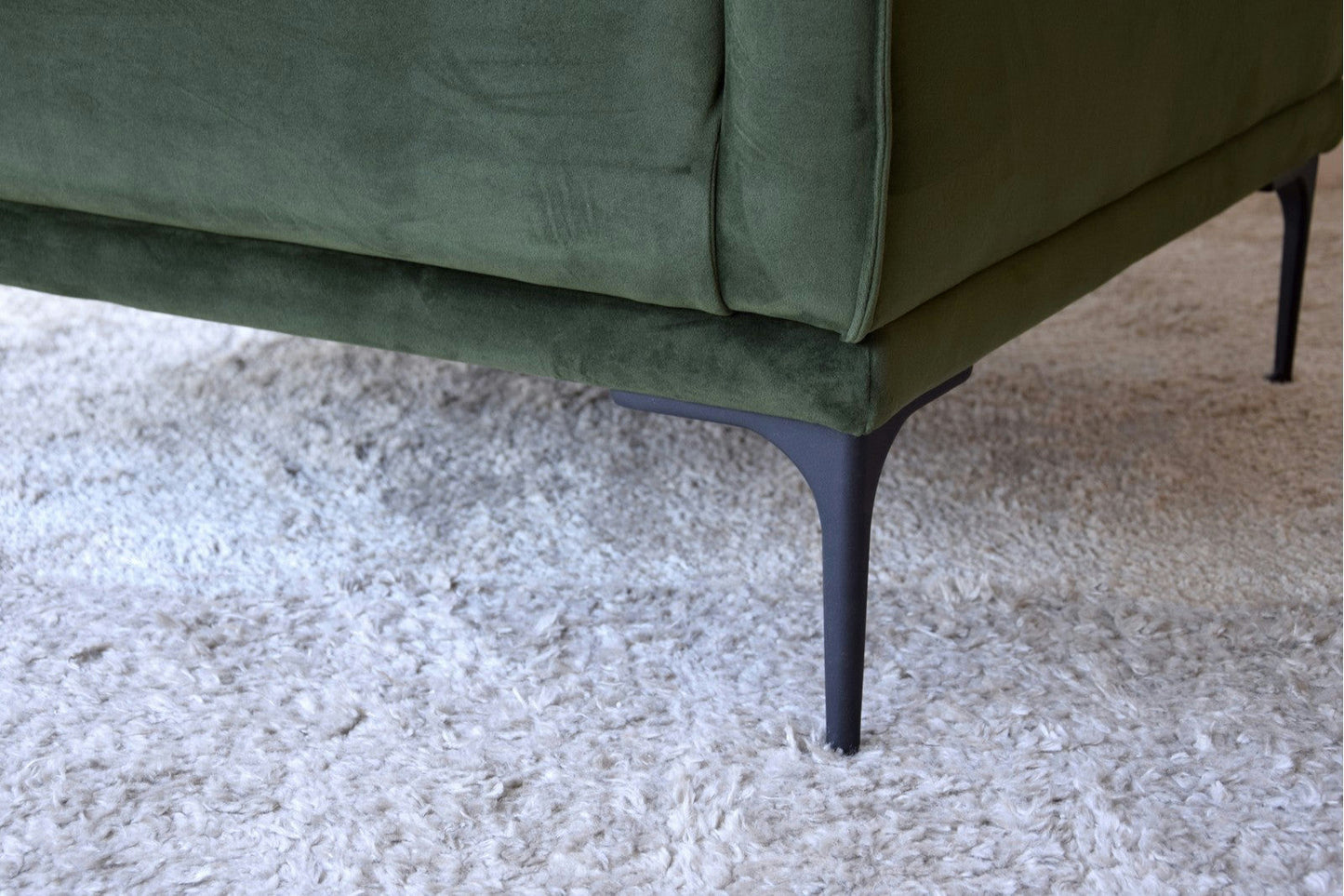 Primer plano de la esquina inferior de un Sillón de Diseño en Terciopelo Ntsu verde con patas metálicas, descansando elegantemente sobre una alfombra de textura ligera.